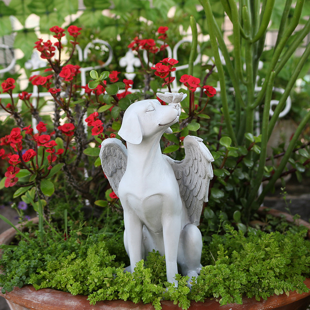 White angel dog memorial statue displayed among red flowers